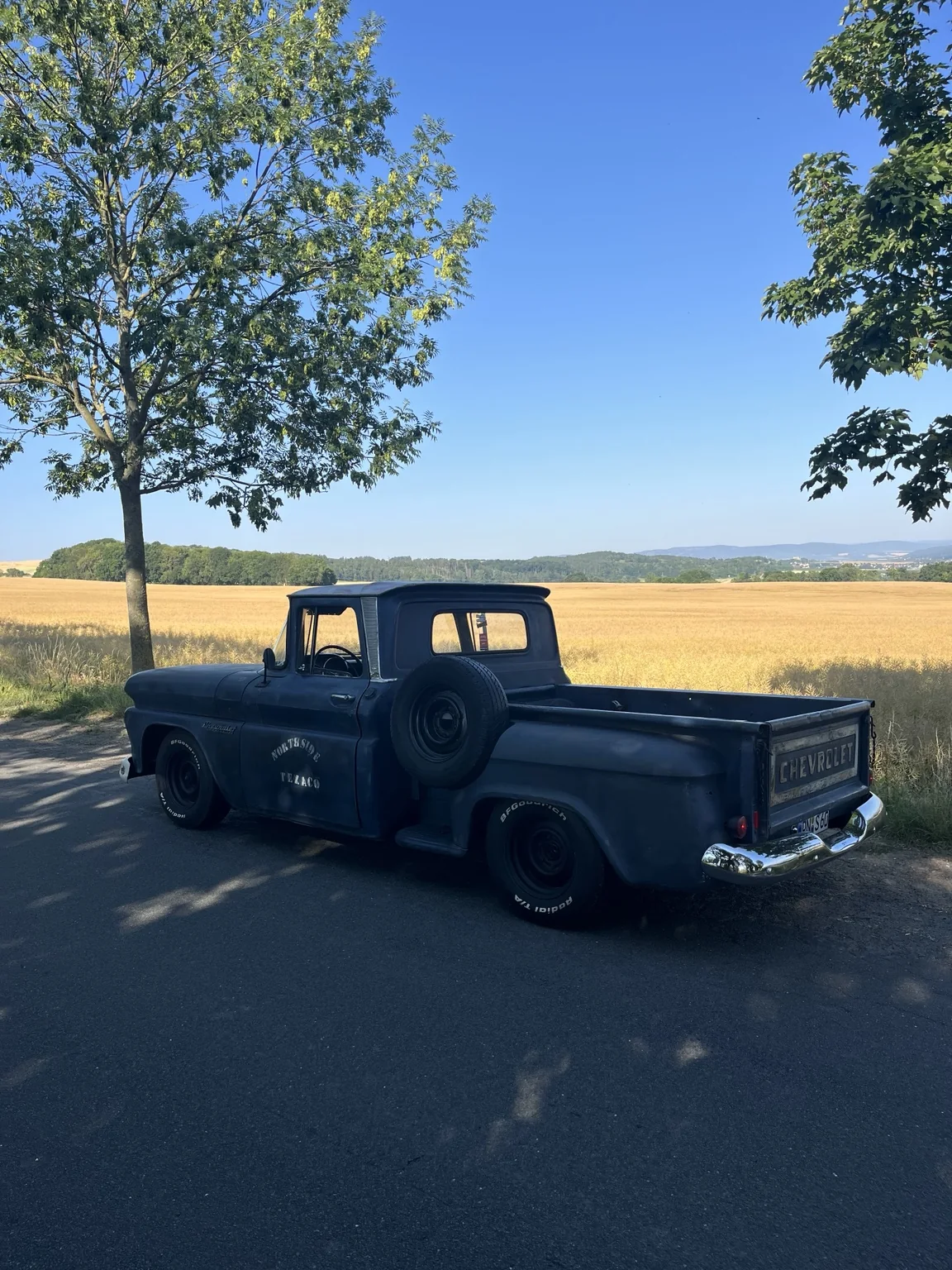 Unser blauer Chevrolet Apache Shortbed von 1960 mit Patina und seitlichem Ersatzrad vor einem sommerlichen Getreidefeld