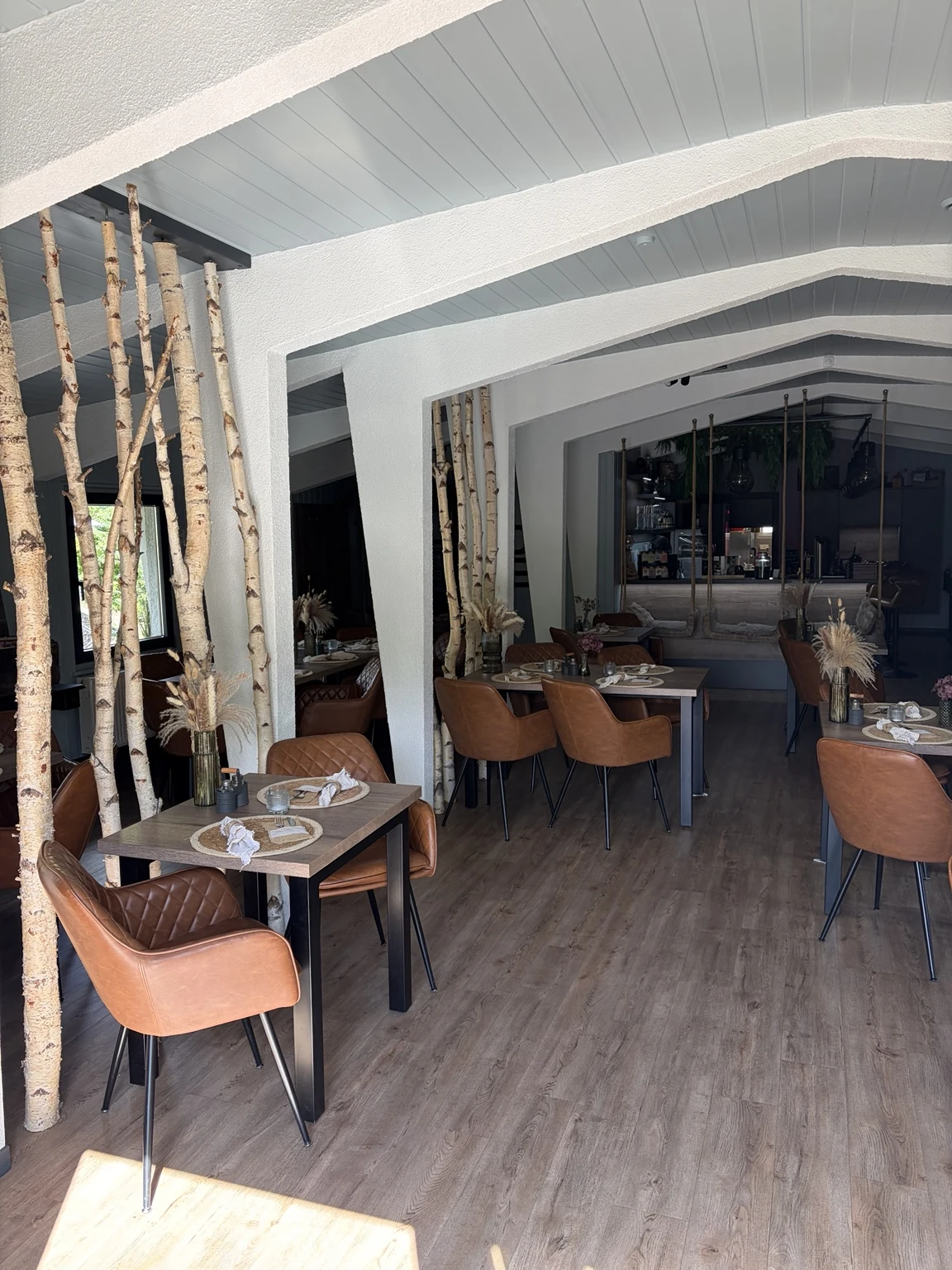 Birch stems, wooden tables and cognac-colored chairs in the real restaurant
