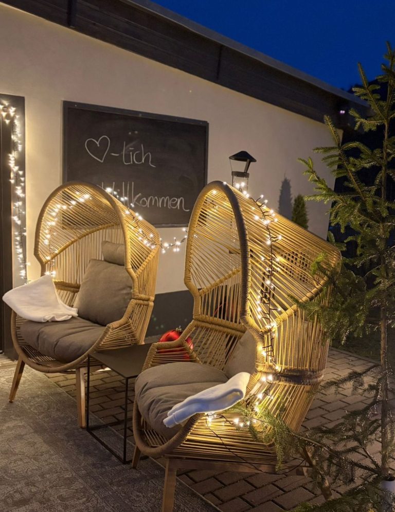 Zwei gemütliche Korbsessel mit Lichtern vor einer Wandtafel im Freien.